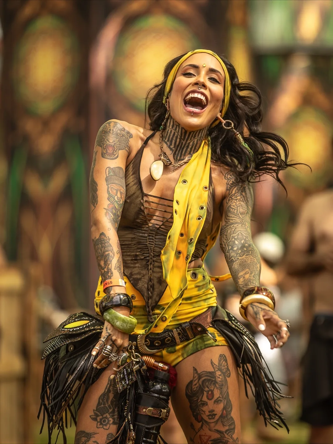 Sophie sorrindo na Árvore da Vida, com lenço amarelo e look de festival